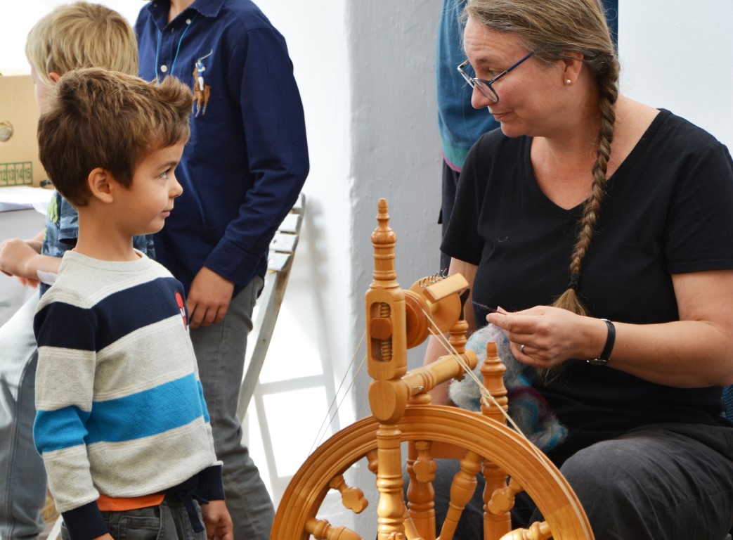 Kind beobachtet Frau am Spinnrad